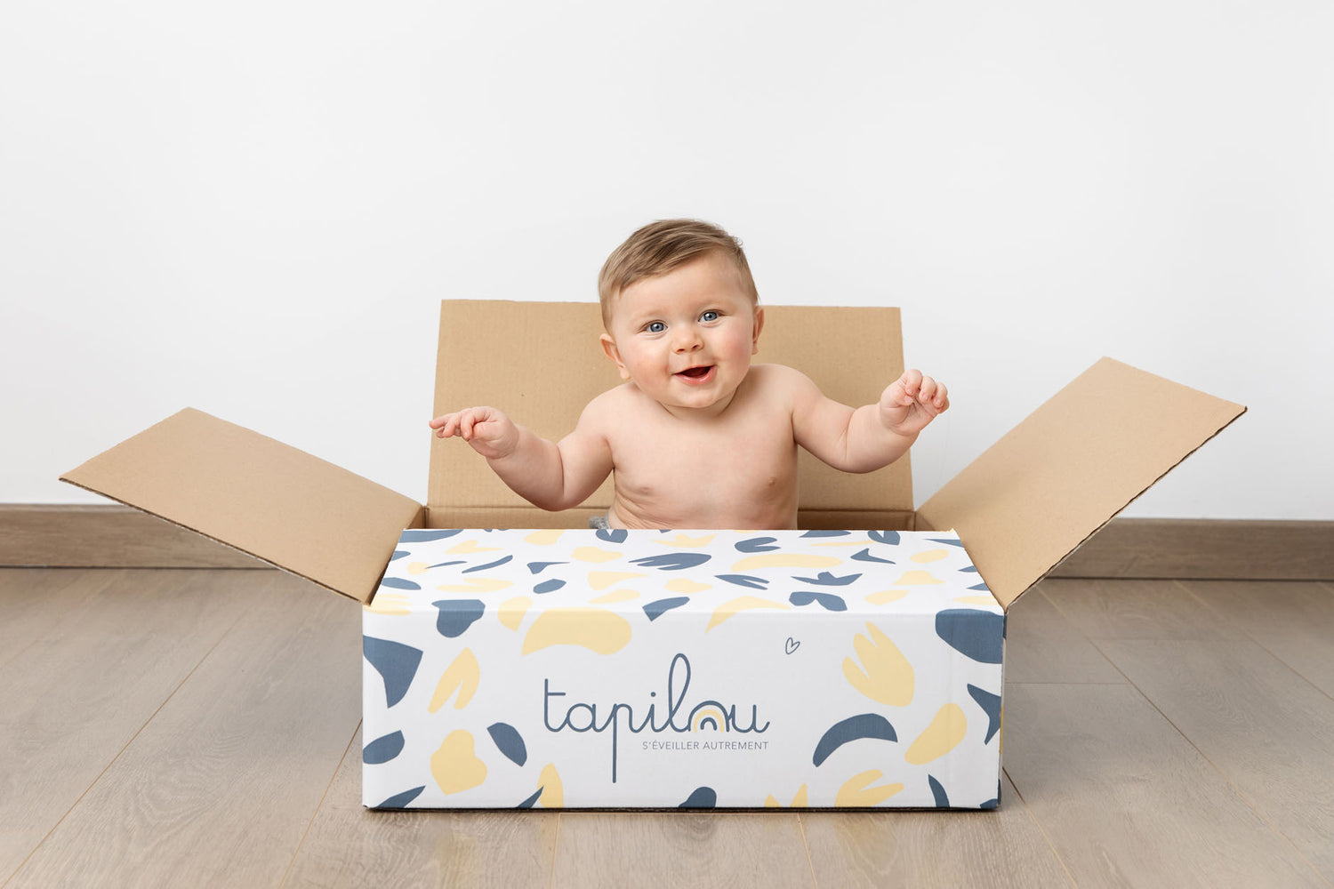 bébé dans un carton tapilou qui rigole