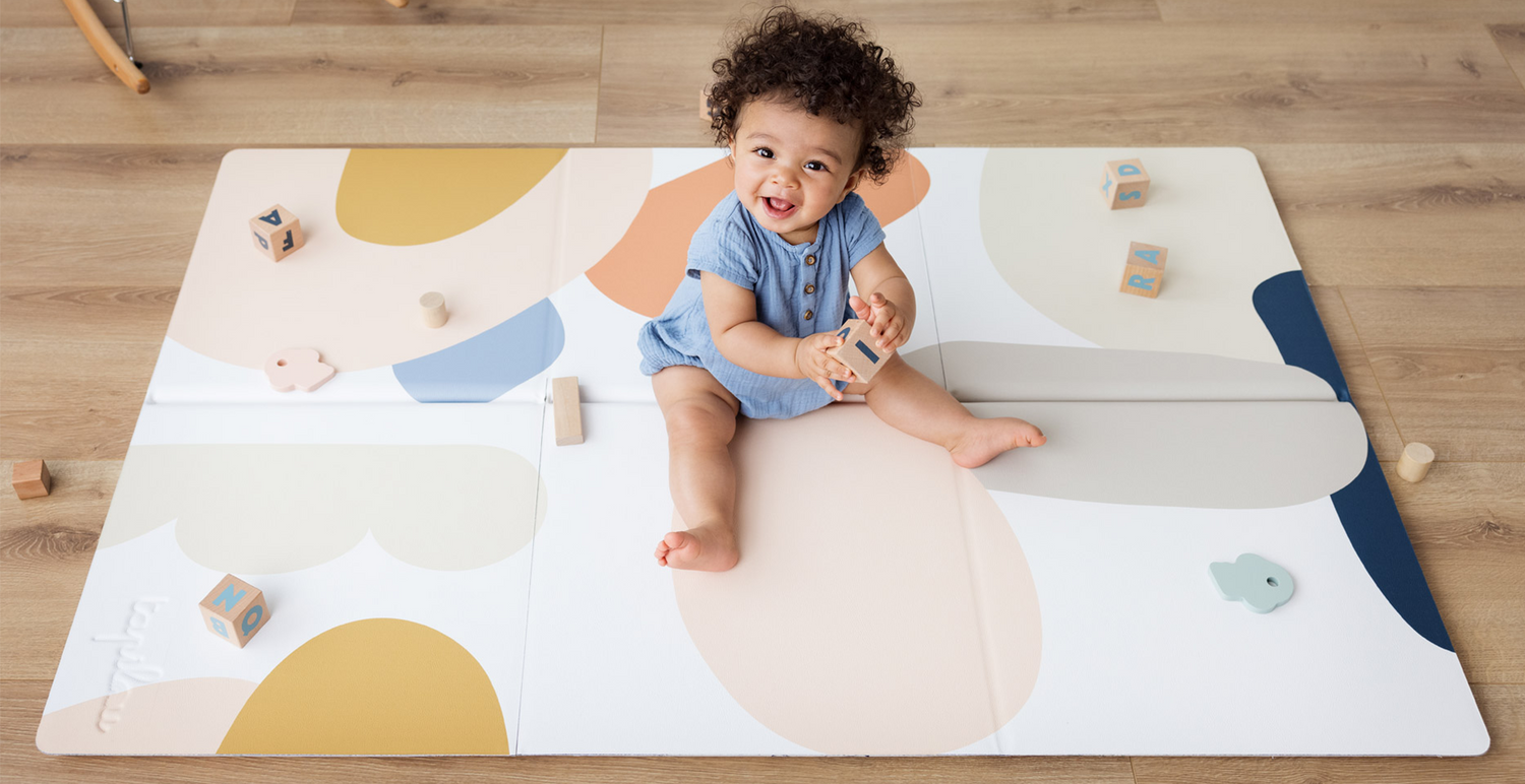 Bébé riant et jouant sur le tapis de jeu Tapilou avec des jouets colorés.